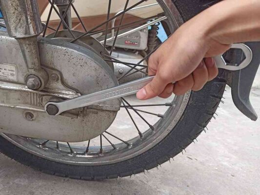 Dùng cờ lê và mỏ lết để nới trục bánh sau và tăng sên cho xe máy 